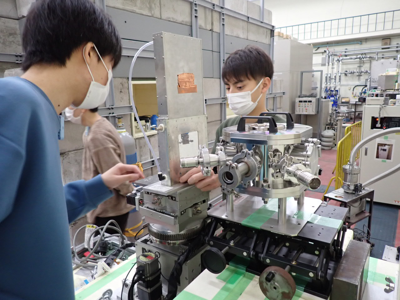 中性子を利用したサーモグラフィの実証実験の準備の様子。測定試料を格納する真空チャンバーと中性子イメージング検出器の準備を研究室の学生さん達が手伝っています。この実験は大変でしたが、担当学生さんの頑張りもあり、その後の実験データ解析や考察、学術論文化を経て、最終的には報道発表に至りました。