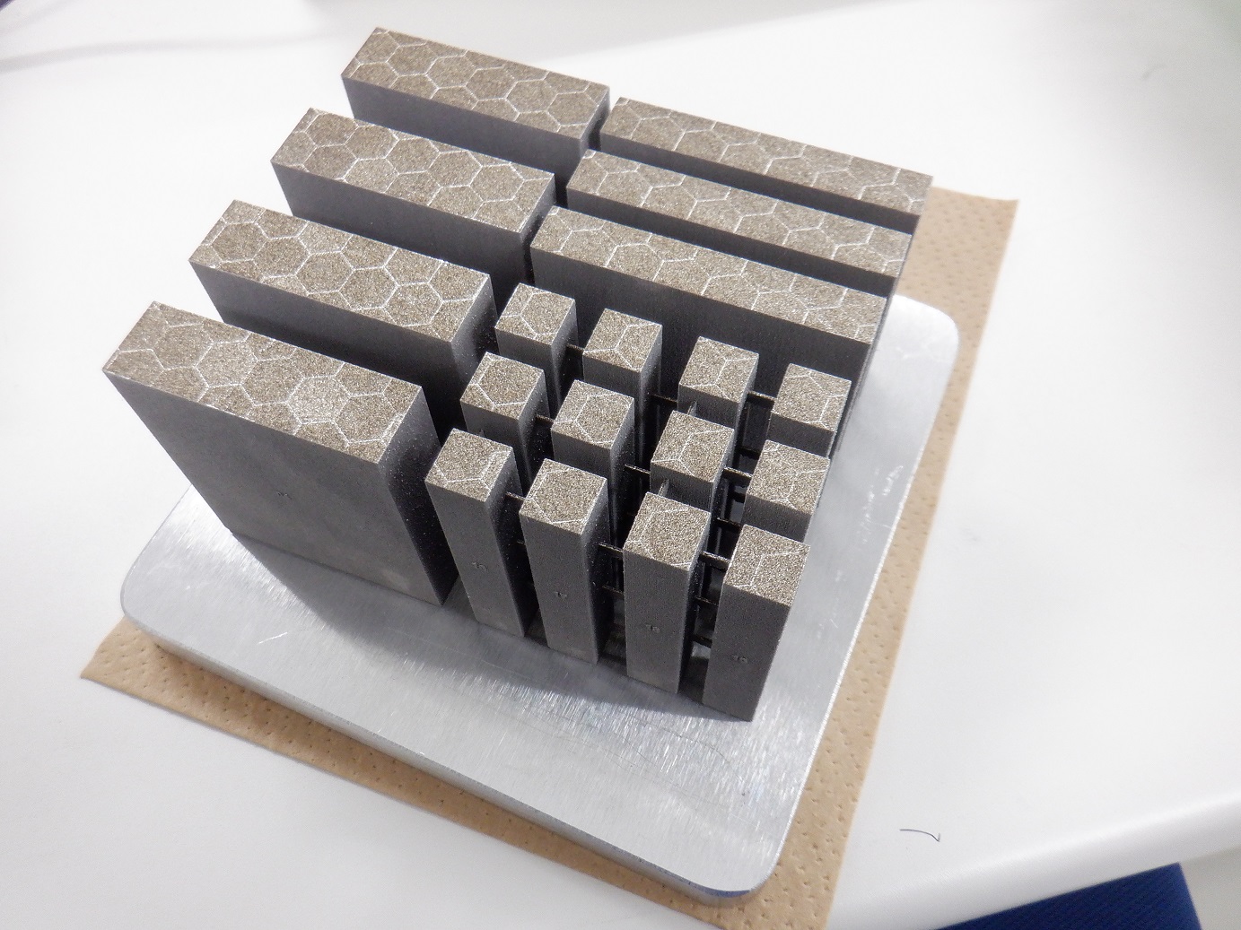 新たに設計した材料を金属3Dプリンタで造った積層造形体(表面の六角形のマークは、レーザー照射のパターンを示す)