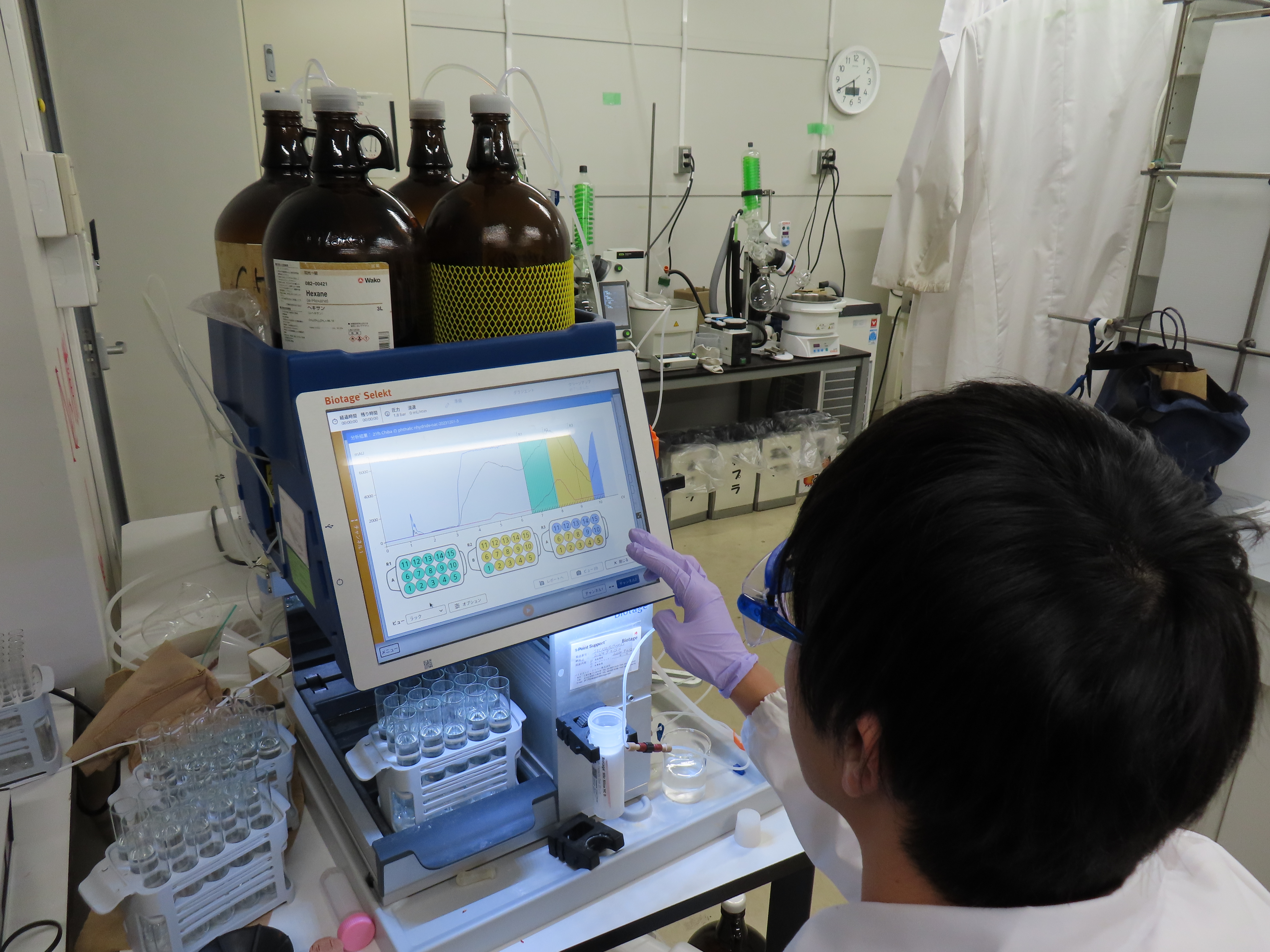 合成した高分子の原料（モノマー）をクロマトグラフィーで精製中。タッチパネルのPCに実験条件を入力すると、全自動で試料を分離し、目的物質が試験管に回収されます。