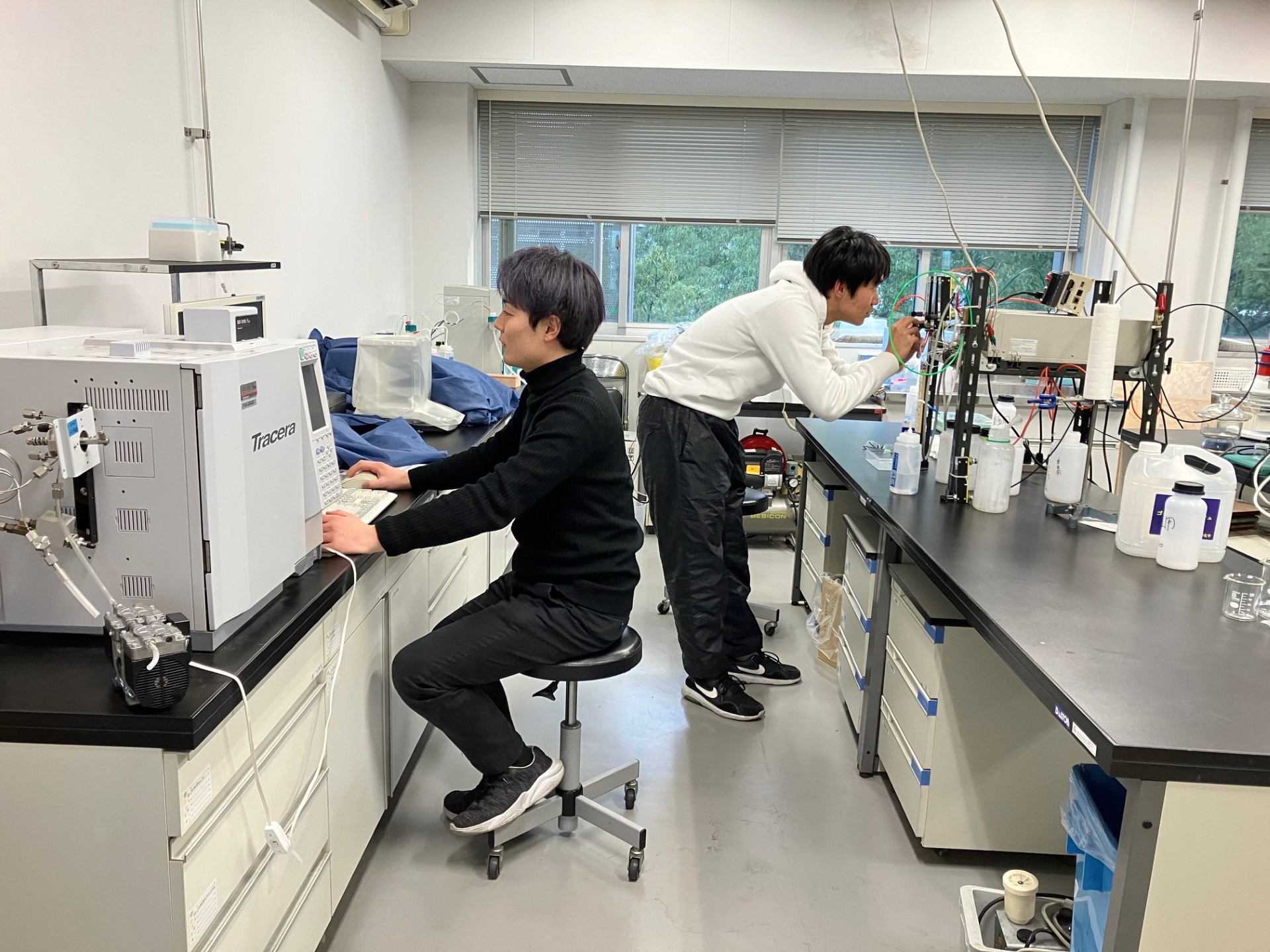 水と二酸化炭素を電気を使って反応させ(奥側の学生)、生成物の定量(手前の学生)をしています。