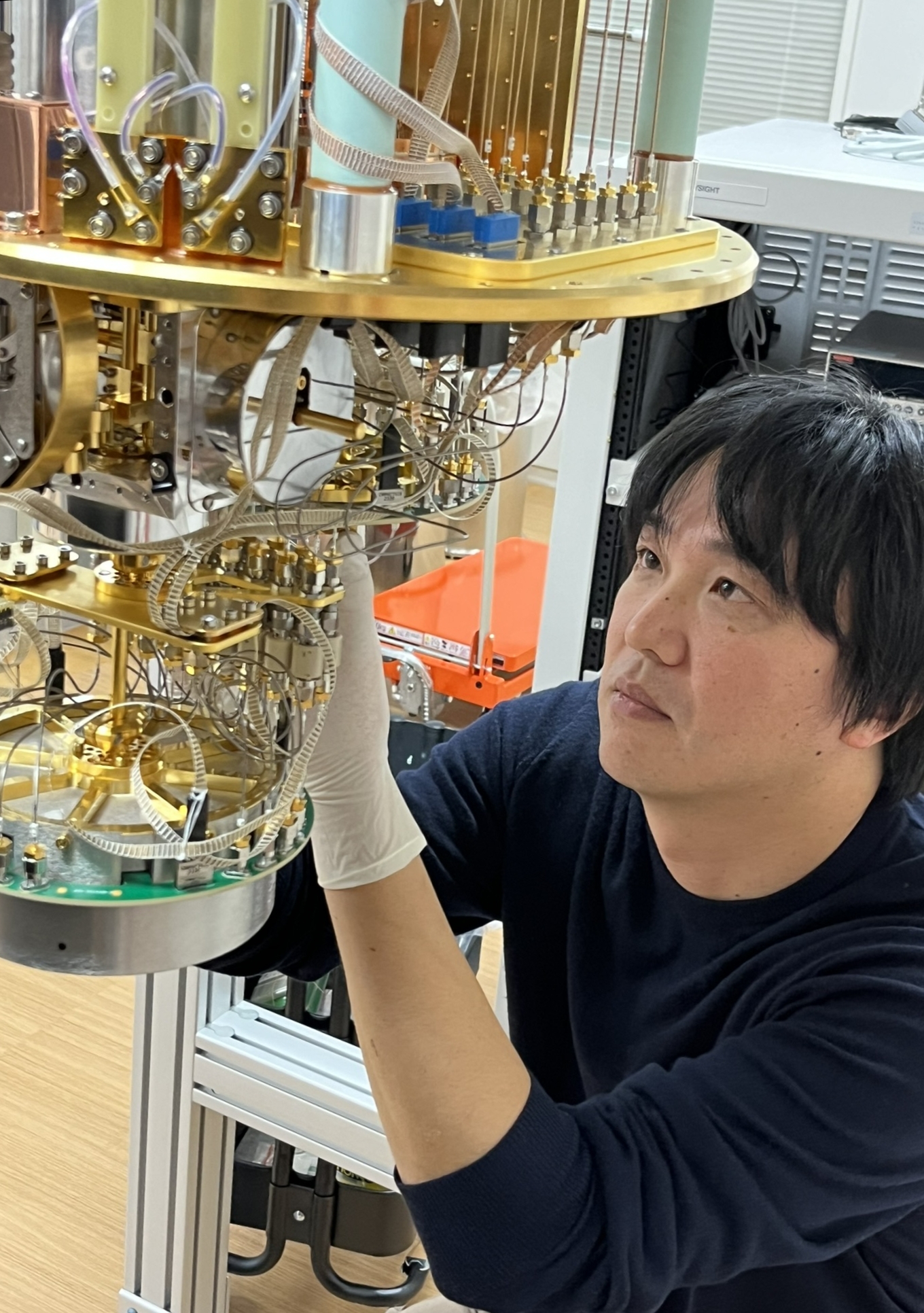 極低温（-273℃）に冷却する冷凍機を用いて量子ビット制御回路の測定を行います。写真は試作した量子ビット制御回路のチップを極低温冷凍機に取り付けているところです。