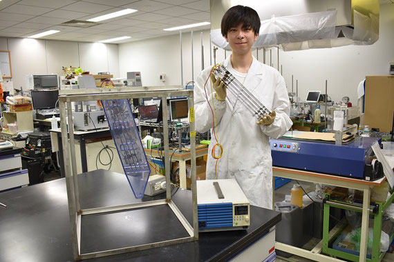 学生が持っているのが、装置の中に入っているものと同じ多層傾斜板電極と呼ばれる装置です。中央の装置にスラリー(固体粒子が液体中に懸濁しているもの)を入れて電圧を加えます。