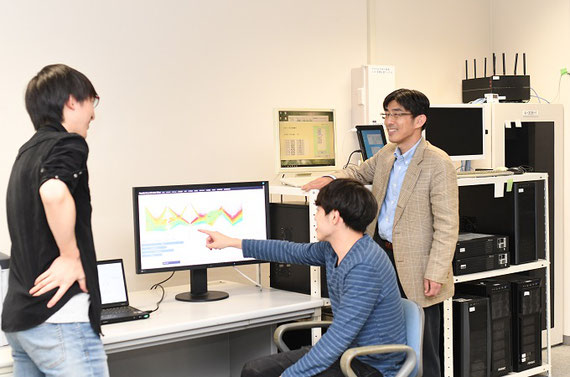 研究室でデータ分析をしています。背後に見えるコンピューター（データベースサーバ群）の電源はEVから給電されています。