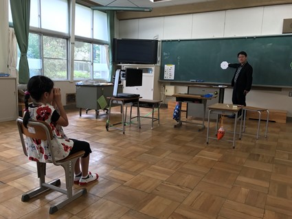 愛知県の小学校で弱視の児童の指導を行なっている様子。弱視にとって見やすい環境を構築することが、我が研究室でのテーマの一つです。見えにくさを抱える児童生徒が通う学校から、来校しての指導を依頼されることも多くあります。この写真のように直接指導をすることもあります。この写真は、小学校で学ぶ見えにくさのある小学生が遠くを大きくして見るための道具（単眼鏡）の操作を習得する方法を直接指導し、学校での日々の指導に生かすために、その様子を担任の先生がご覧になっている様子です。