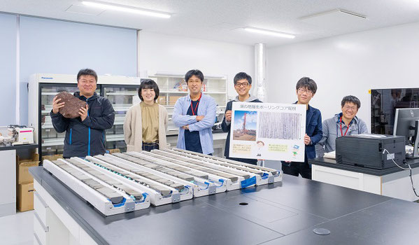 １億年前の年縞が保存されている湖の地層の堆積物コアを前に、研究室の学生との集合写真。高知大学海洋コア総合研究センターの分析室にて。右奥にある超高解像度分析装置（XRFコアスキャナー）を用いて、１億年前の気候変動の実態を探っています。